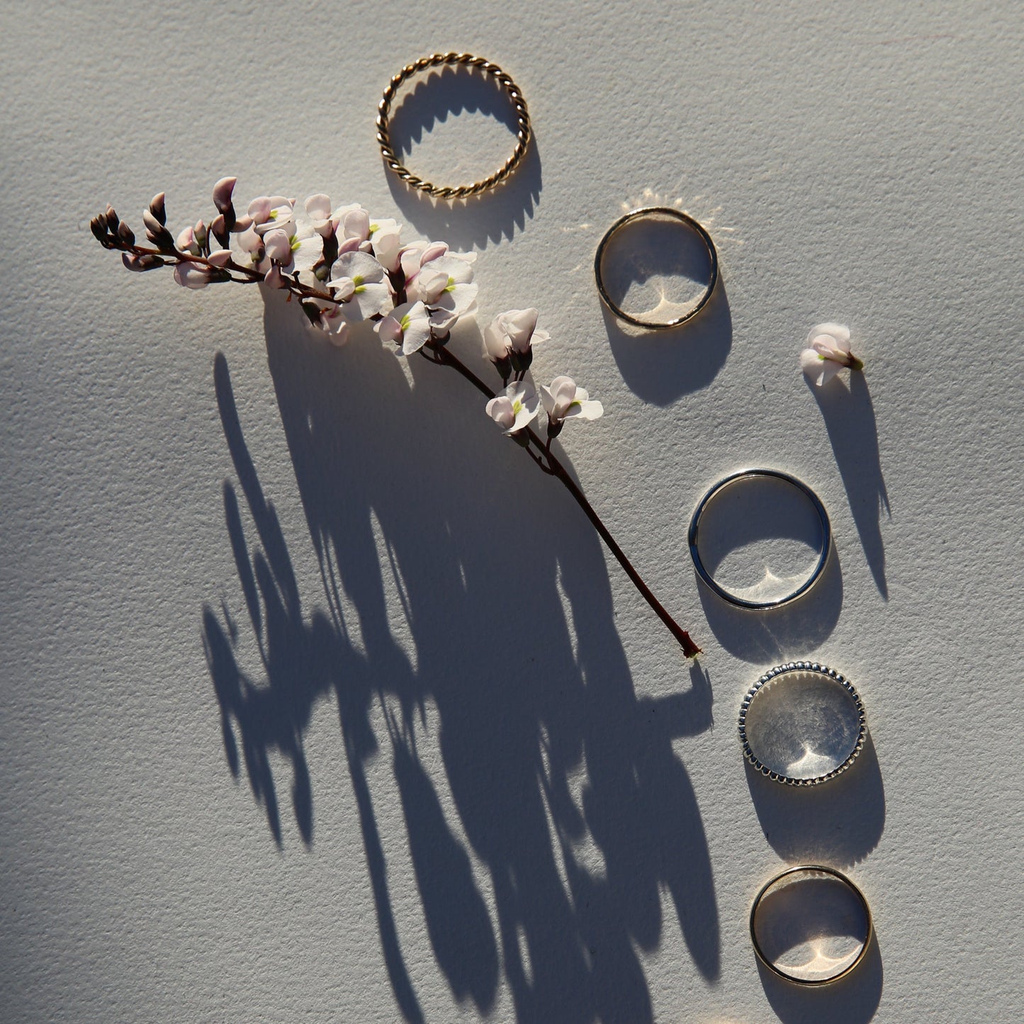 Gold rings and a branch with small flowers on a gray surface