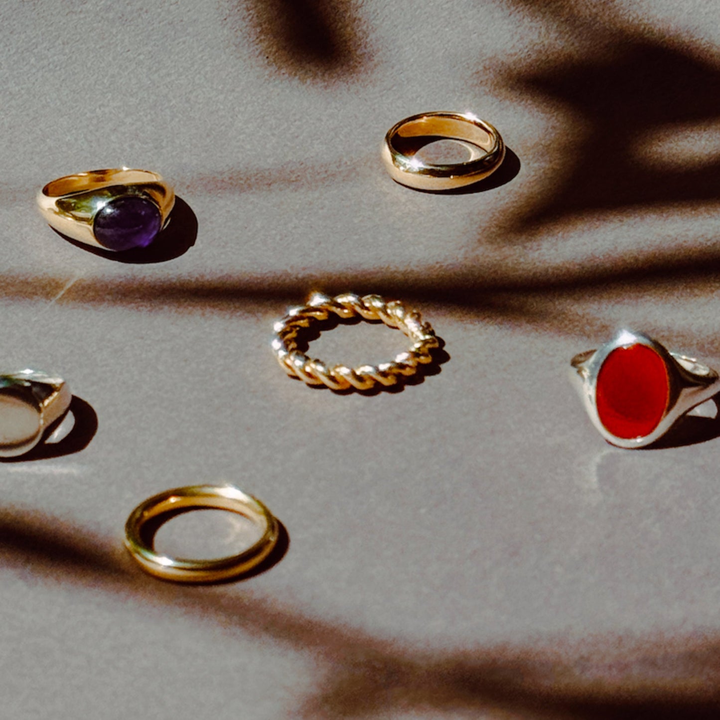 A collection of various rings displayed on a textured surface, including a chunky twist ring.