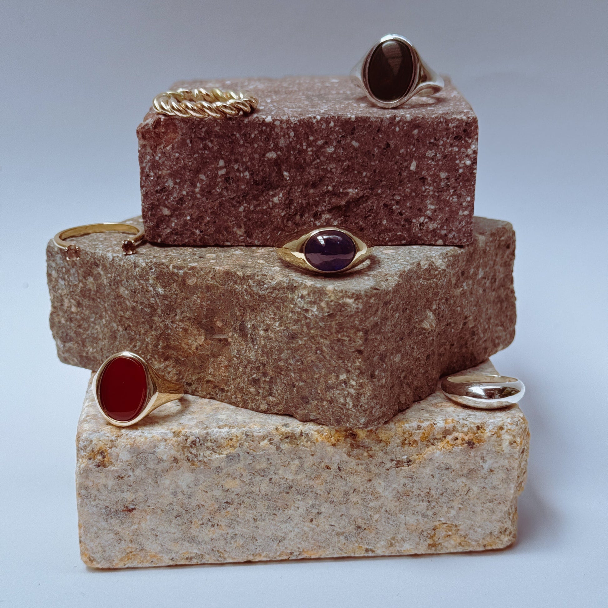 A selection of rings against a light blue backdrop sitting atop of different pieces of rocks