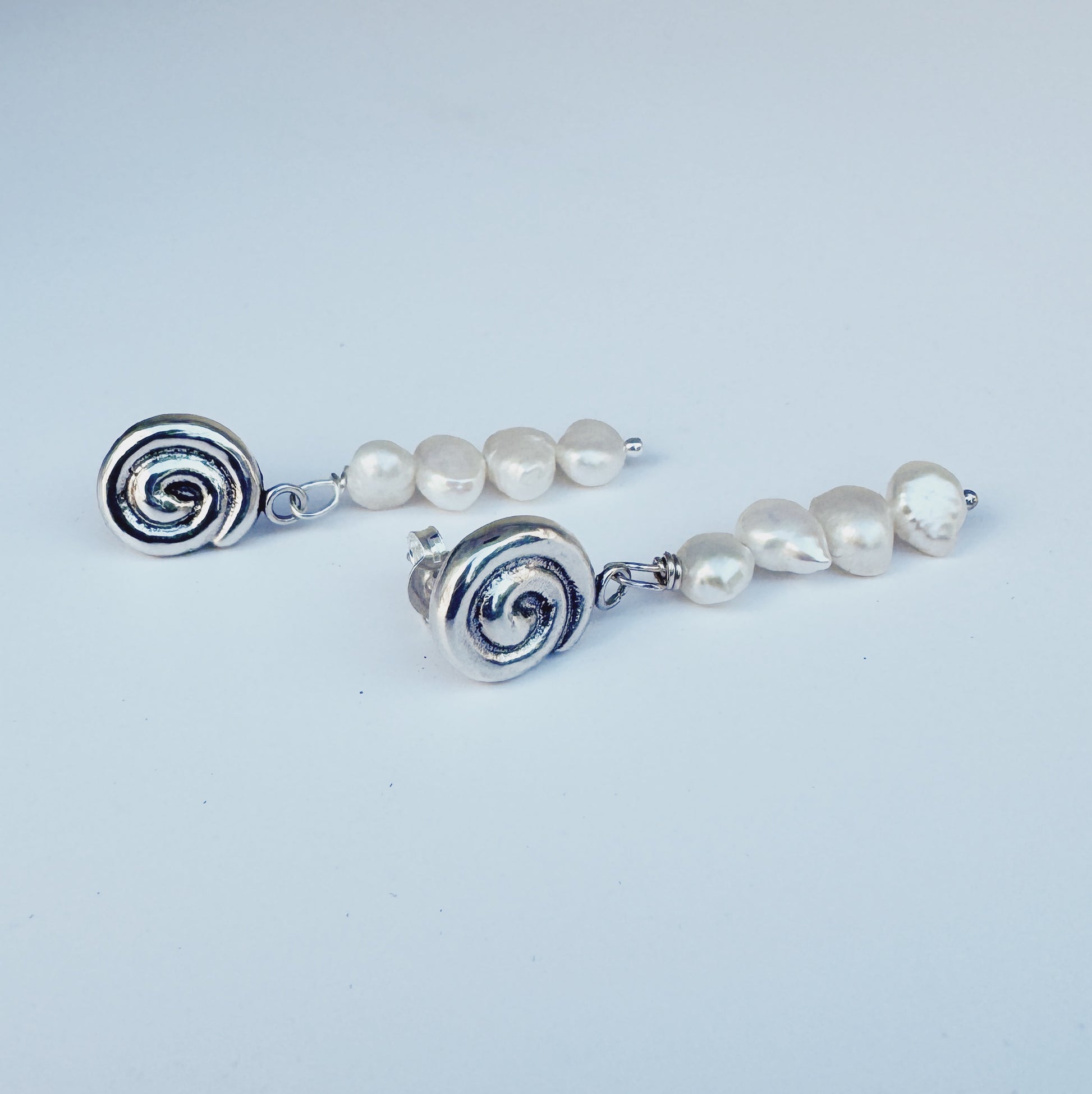 Pair of earrings with silver spiral ends and pearl beads on a light blue background