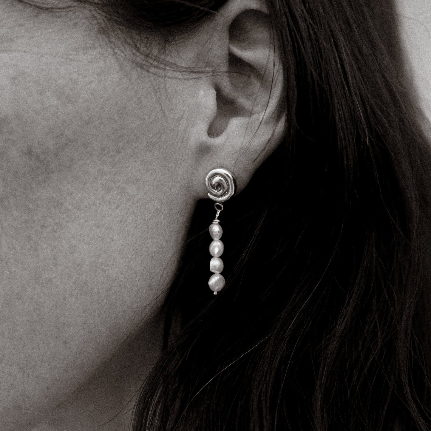 Close-up of an earring with pearls worn by a person.