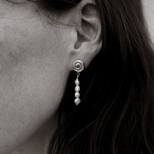 Close-up of an earring with pearls worn by a person.