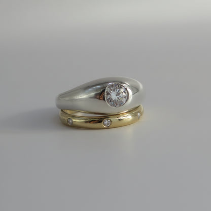 A two-tone wedding ring set featuring a silver band with a round clear gemstone and a yellow gold band with small inset diamonds, displayed on a neutral gray background.