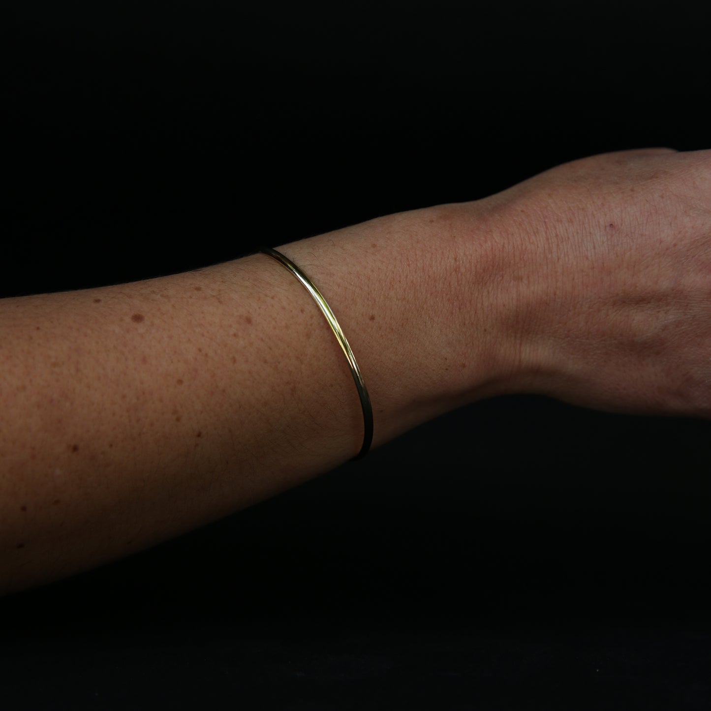 Gold bracelet on a person's wrist against a black background