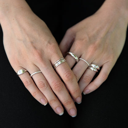 Close-up of hands wearing multiple silver rings on a black background