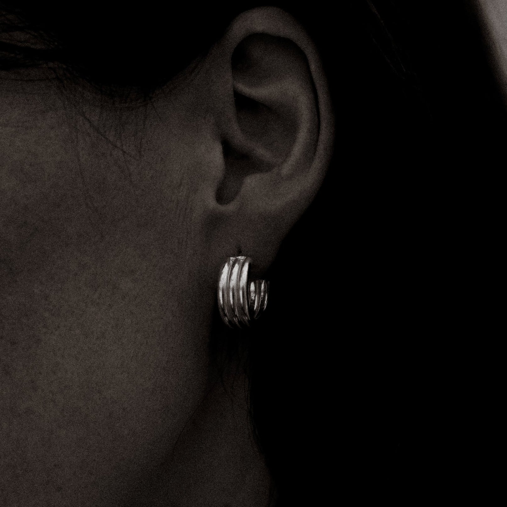 Close-up of an ear wearing a silver hoop earring with a blurred background