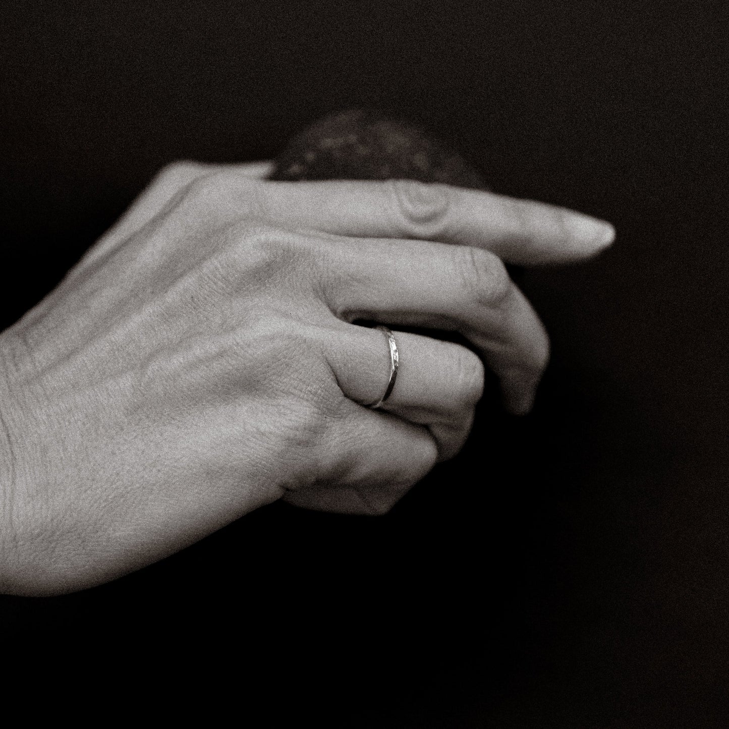 Black and white photo of a hand with a ring on a dark background