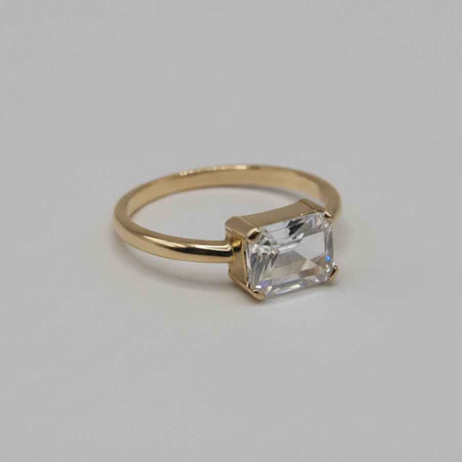 Gold ring with an emerald cut diamond on a light gray background