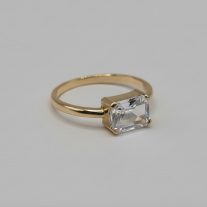 Gold ring with an emerald cut diamond on a light gray background