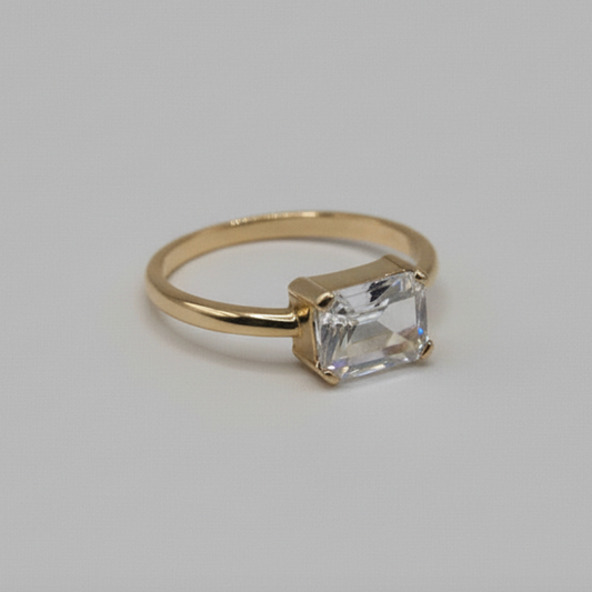 Gold ring with an emerald cut diamond on a light gray background