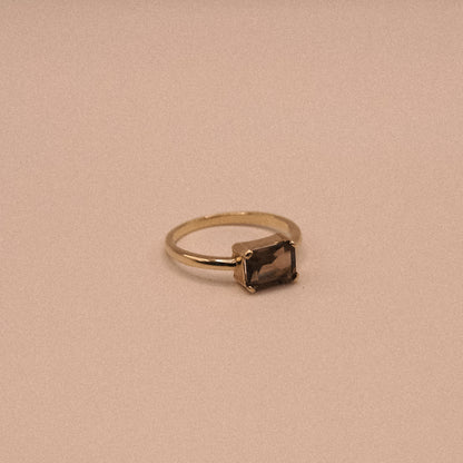 Gold ring with a rectangular gemstone on a beige background