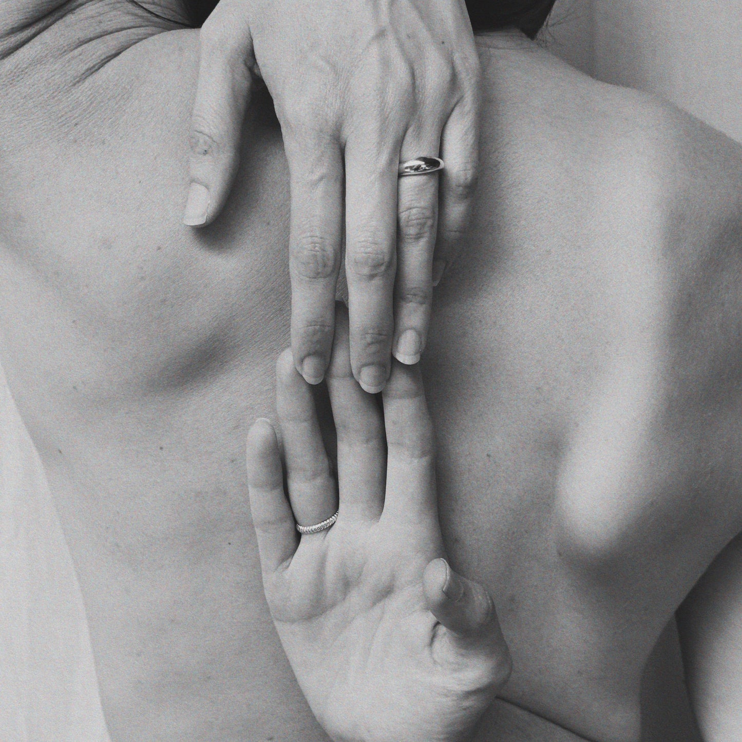 A black and white image of a hand with a ring on the finger, touching the back of another hand.