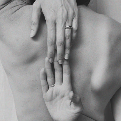 A black and white image of a hand with a ring on the finger, touching the back of another hand.