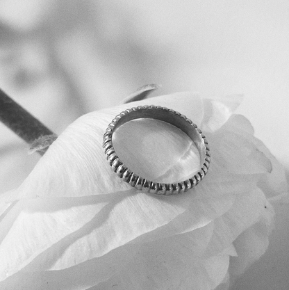 black and white image of a silver ring with line detail sitting atop a white flower.