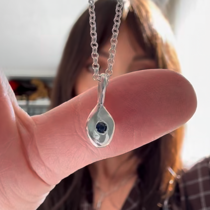 Silver teardrop pendant with a blue gemstone held between fingers