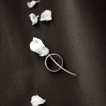 Silver ring with white floral design on a dark fabric background