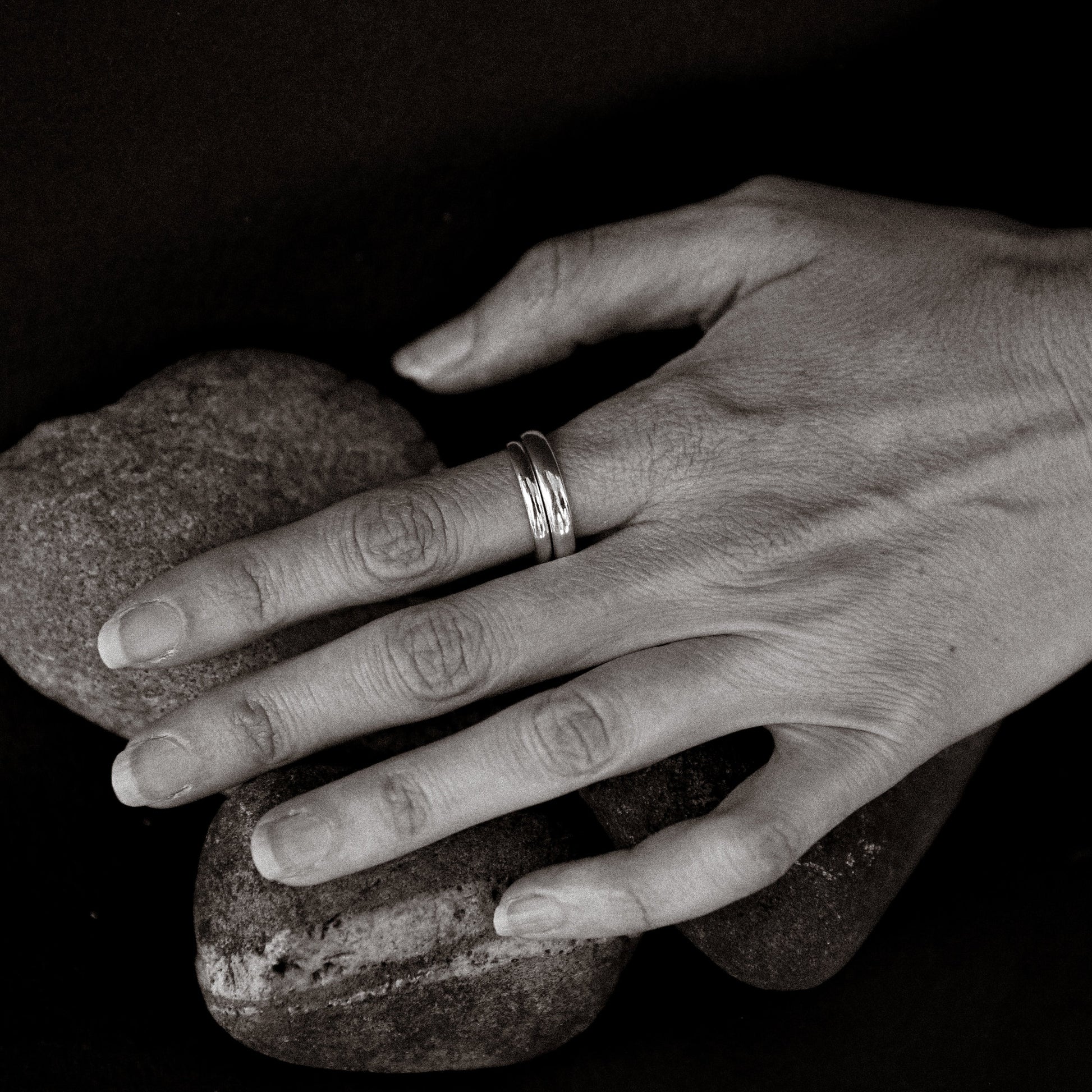 Hand holding two rocks with a ring on a dark background