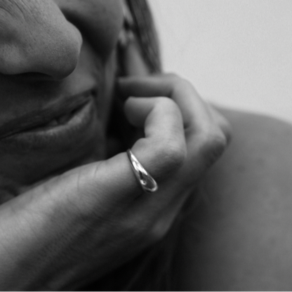 black and white image of a womans smile with her hand on her face with a silver ring on