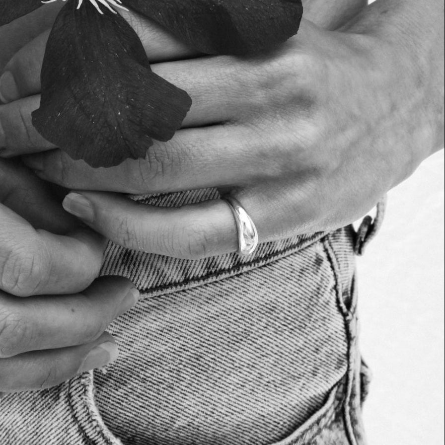 A black and white image of a person's hands holding a flower, wearing a ring on one of their fingers.