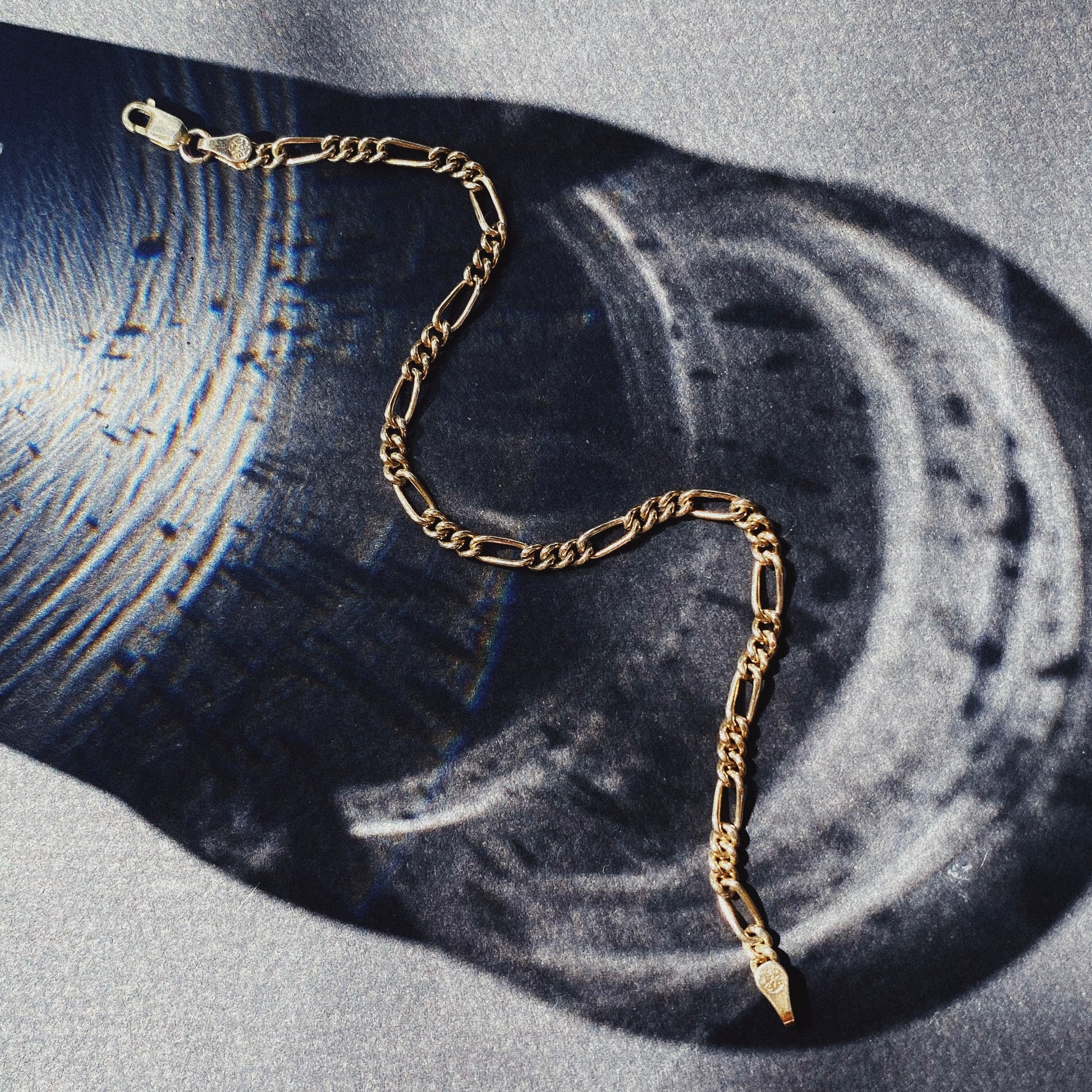 A gold Figaro chain bracelet displayed on a flat surface.