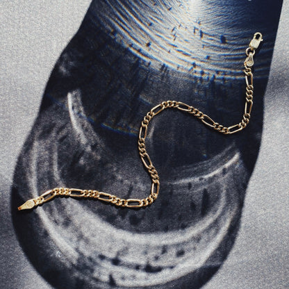 A gold Figaro chain bracelet displayed on a flat surface.