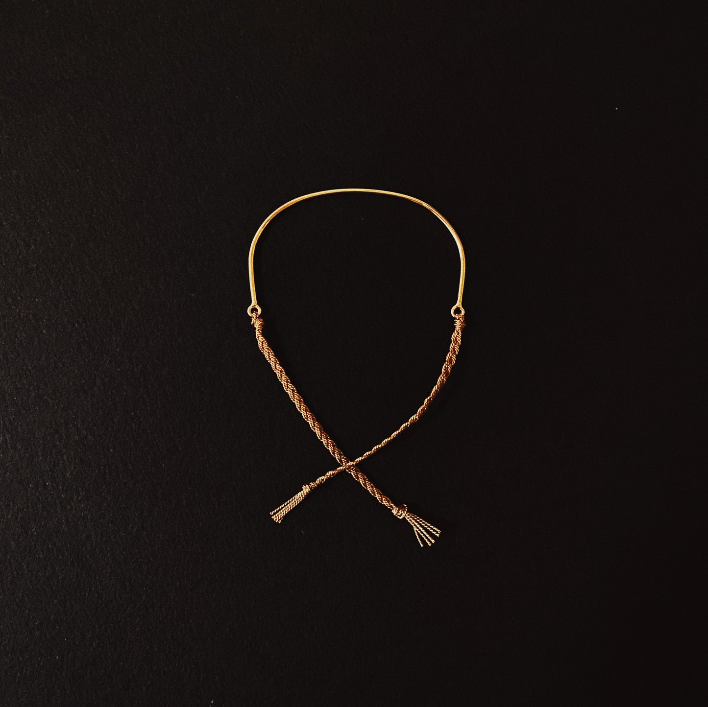 A bracelet made of sterling silver or solid 9ct yellow gold with a hand braided silk tie, displayed against a black background.