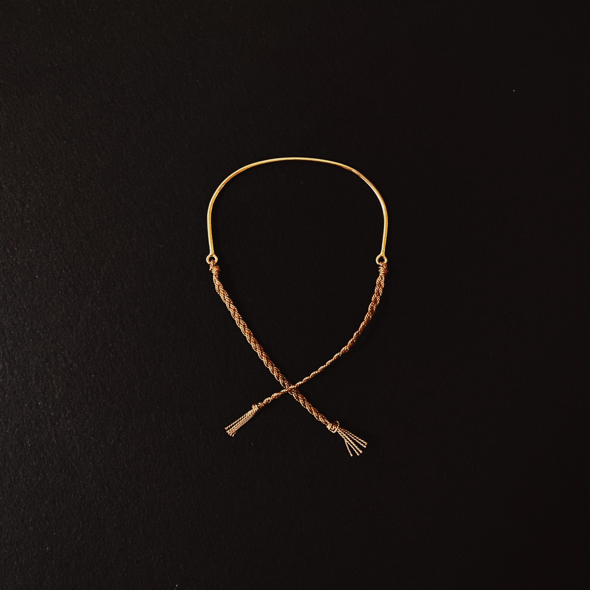 A bracelet made of sterling silver or solid 9ct yellow gold with a hand braided silk tie, displayed against a black background.