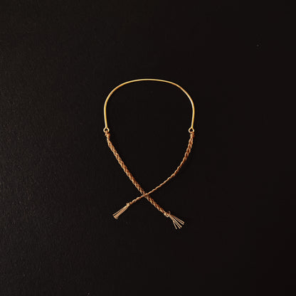 A bracelet made of sterling silver or solid 9ct yellow gold with a hand braided silk tie, displayed against a black background.