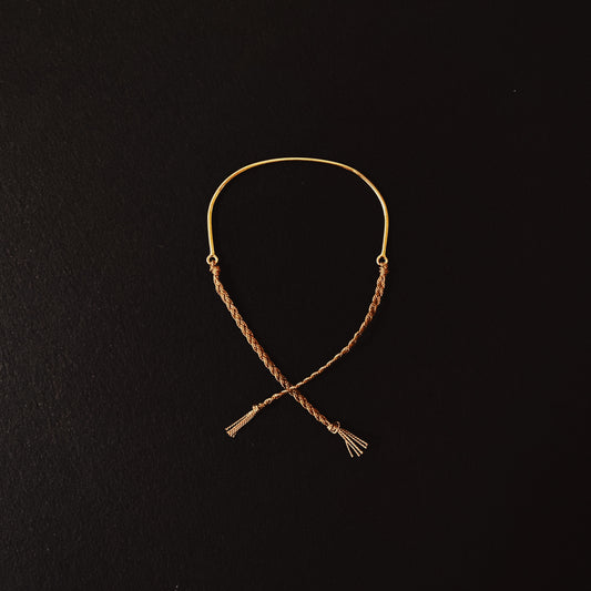 A bracelet made of sterling silver or solid 9ct yellow gold with a hand braided silk tie, displayed against a black background.
