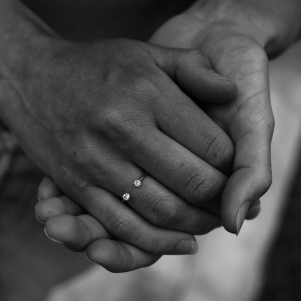 Close-up of a hand wearing a ring with two stones on a blurred background.