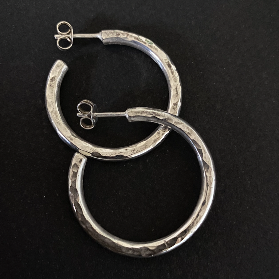 An closeup image of a pair of silver textured hoops on a black background.