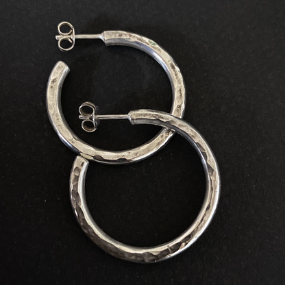 An closeup image of a pair of silver textured hoops on a black background.
