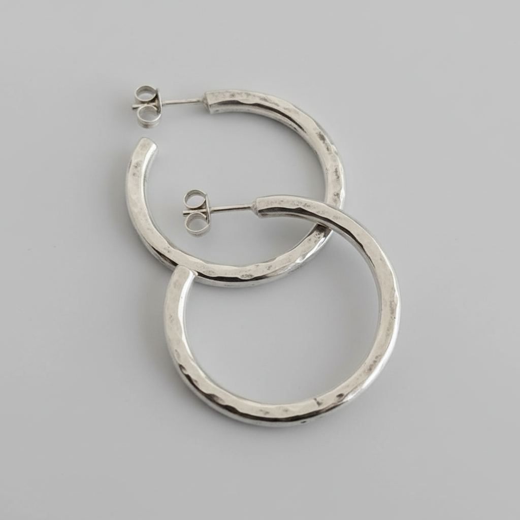 An closeup image of a pair of silver textured hoops on a light grey background.
