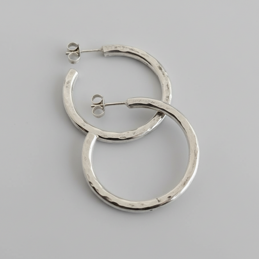 An closeup image of a pair of silver textured hoops on a light grey background.