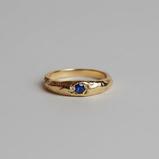 Gold ring with a blue gemstone on a grey studio background