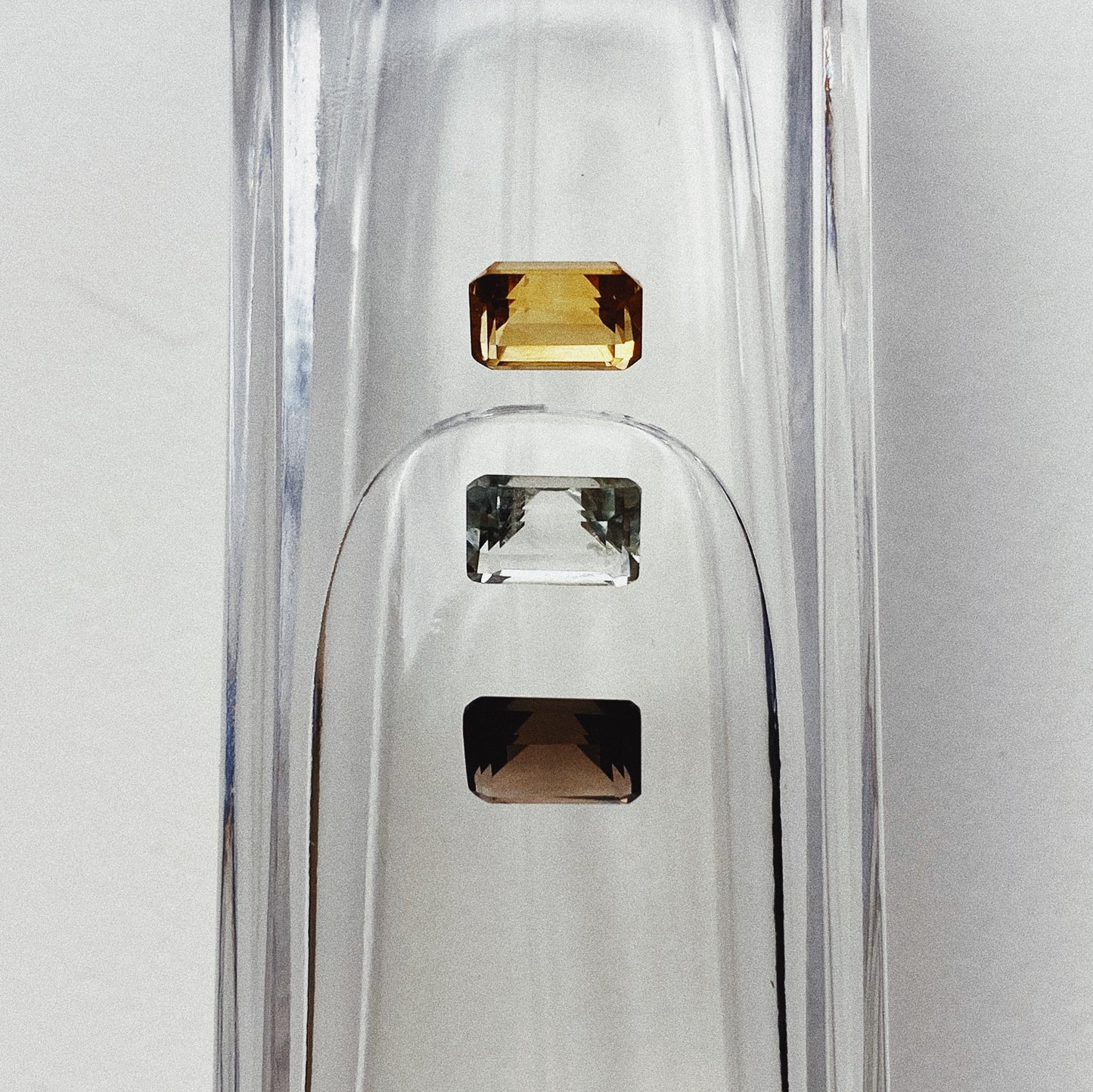 Three emerald cut stones - a citrine, mint quartz and smoky quartz sitting atop a water filled vessel.