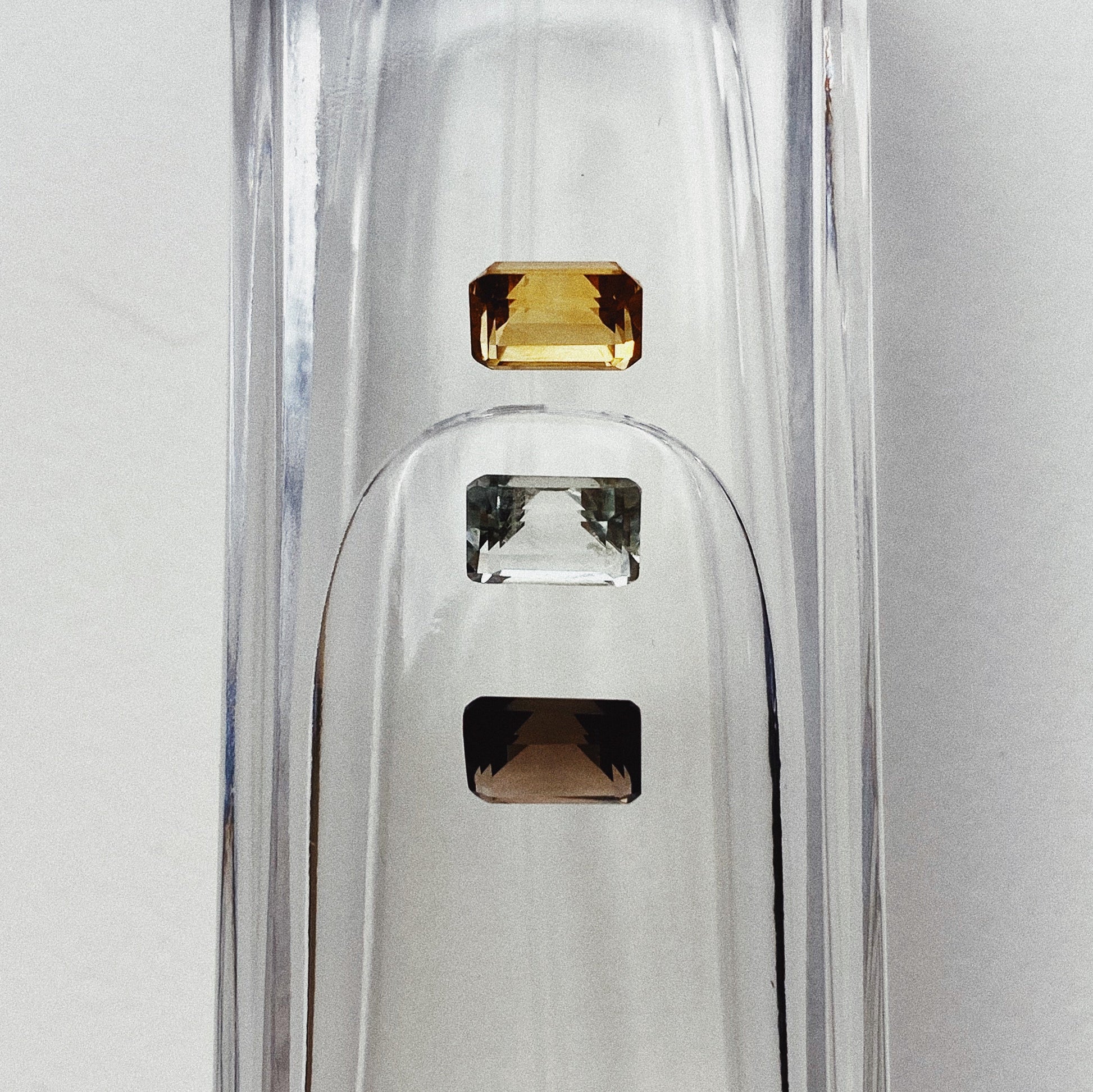 Three emerald cut stones - a citrine, mint quartz and smoky quartz sitting atop a water filled vessel.