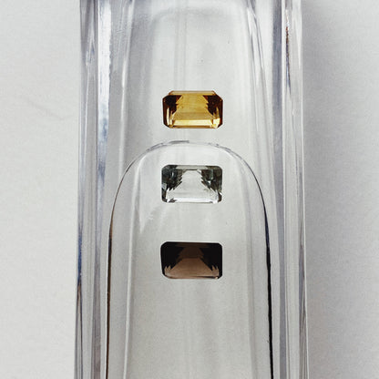 Three emerald cut stones - a citrine, mint quartz and smoky quartz sitting atop a water filled vessel.